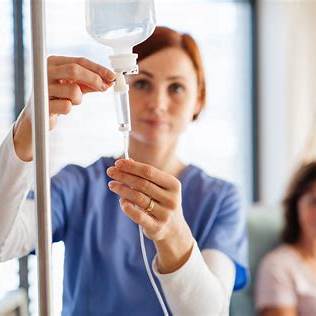 Alt Text: Ärztin bereitet Infusionsbehandlung vor mit Tropf und Patient im Hintergrund.