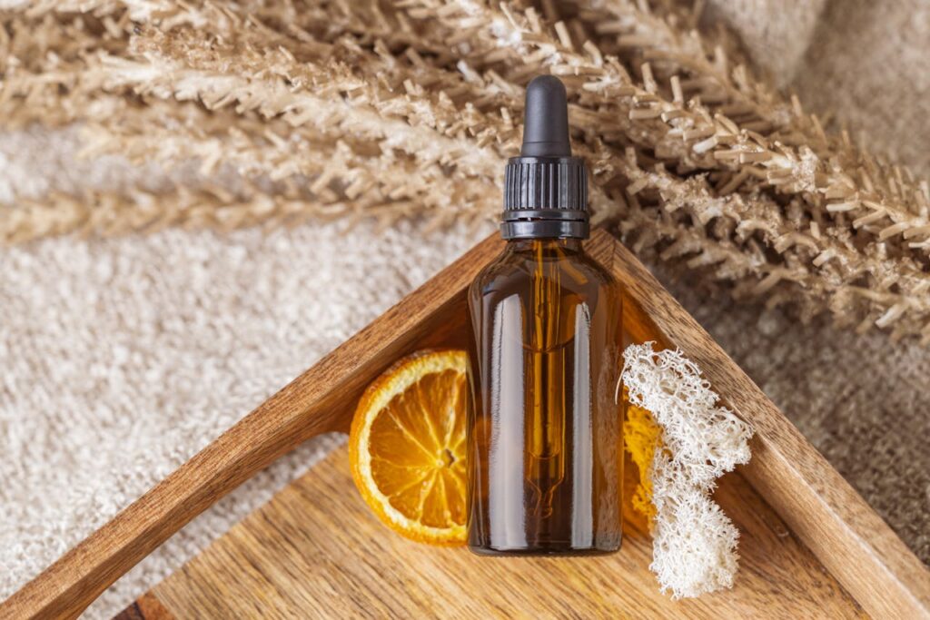 Braune Flasche mit Vitamin-C-Serum und getrockneter Orange auf Holzunterlage.